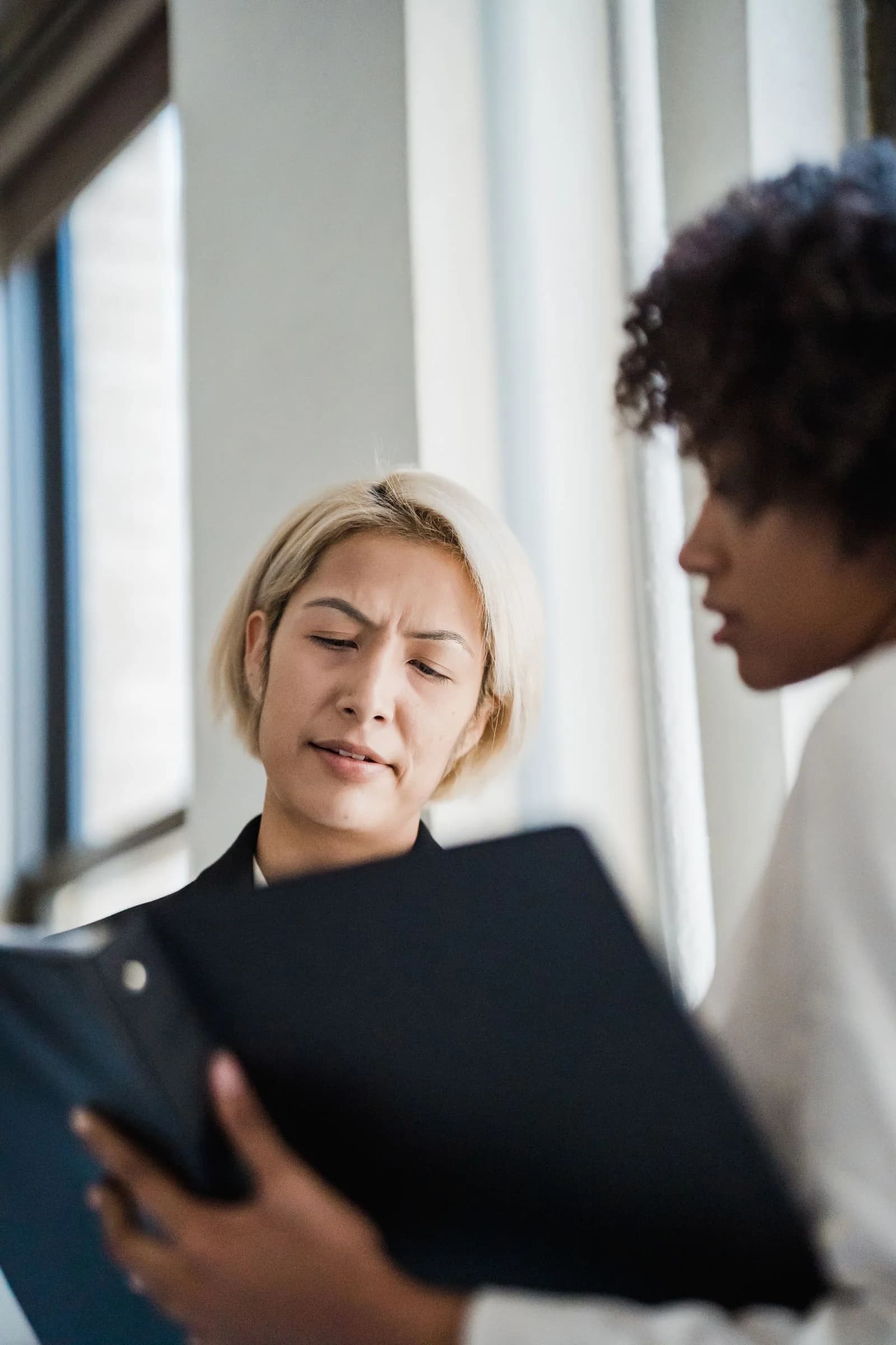 Two colleagues discussing a document folder in an office.